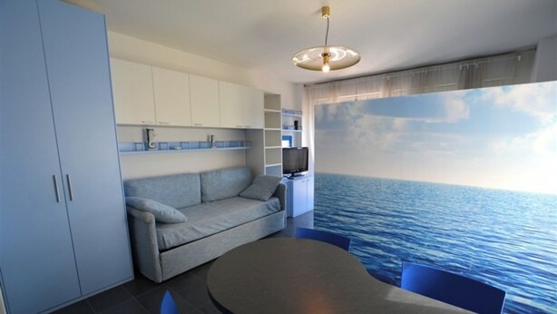 A modern interior with a sofa, a dining table, and a TV. - Nice Studio With sea View Balcony in Lignano Pineta (Lignano Sabbiadoro)