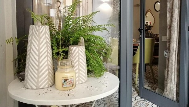 Een tafeltje met twee witte vazen en een kaars, omringd door groene planten.