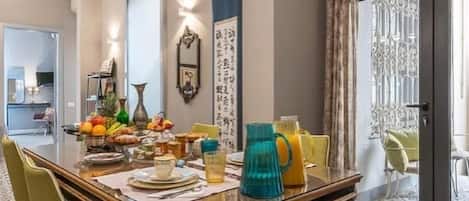 Comedor con una mesa de madera, sillas verdes y un frutero.