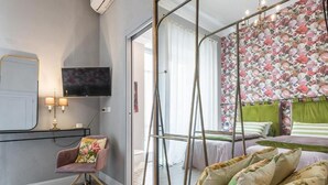 Een moderne slaapkamer met een bed, een stoel, een televisie en een raam met gordijnen.