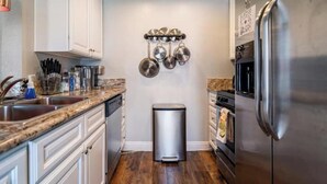 A compact kitchen with white cabinets, a stainless steel refrigerator, and a hanging pot rack. - Charming & Cozy Condo • Pool-Spa & Pac-Man Arcade (Indio)