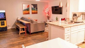 A modern kitchen with white cabinets, a granite countertop, and a built-in oven. There is a dining area with a white table and bench. - Charming & Cozy Condo • Pool-Spa & Pac-Man Arcade (Indio)