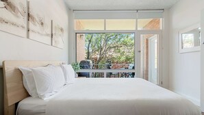 A bedroom with a bed, a nightstand, a window with a view of the outside, and a door leading to another room. - Spacious and Idyllic Unit in Little Manly (Manly)