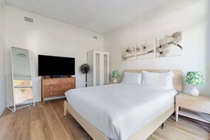 A bedroom with a bed, a TV, a wardrobe, a bedside table, a lamp, and artwork on the wall. - Spacious and Idyllic Unit in Little Manly (Manly)