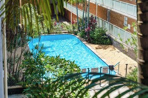 A swimming pool surrounded by lush greenery, with a brick building in the background. - Spacious and Idyllic Unit in Little Manly (Manly)