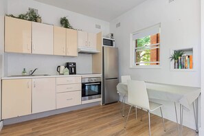 Une cuisine moderne avec des meubles de couleur claire, un réfrigérateur en acier inoxydable, un four, un four à micro-ondes et un coin repas avec une table et des chaises.