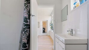 A narrow hallway with a shower curtain, a sink with toiletries, and a mirror. - Spacious and Idyllic Unit in Little Manly (Manly)