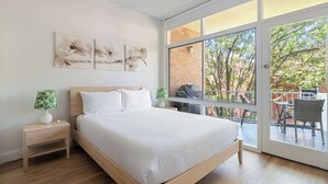 A bedroom with a large window, a bed, a nightstand, and artwork on the wall. - Spacious and Idyllic Unit in Little Manly (Manly)