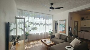 A modern living room with a sofa, coffee table, and a TV. There is a kitchen area with cabinets and appliances. - Spacious and Idyllic Unit in Little Manly (Manly)