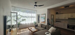 Un salon moderne avec un canapé, une table basse et un téléviseur. Il y a également un coin cuisine équipé de placards et d’appareils électroménagers.