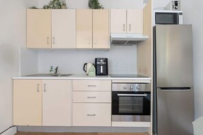 Une cuisine avec des meubles de couleur claire, un réfrigérateur en acier inoxydable, un four à micro-ondes, une machine à café et un four.