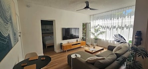 A modern living room with a sofa, coffee table, TV, and a ceiling fan. - Spacious and Idyllic Unit in Little Manly (Manly)