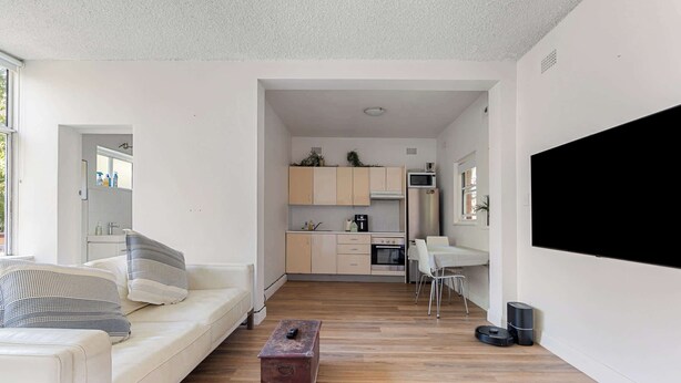 A modern living room with a sofa, a coffee table, and a kitchen in the background. - Spacious and Idyllic Unit in Little Manly (Manly)