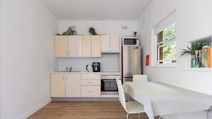 A compact kitchen with a dining table, a refrigerator, a microwave, and a window with a view. - Spacious and Idyllic Unit in Little Manly (Manly)