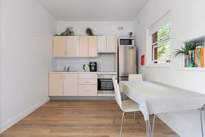 A compact kitchen with a dining table, a refrigerator, a microwave, and a window with a view. - Spacious and Idyllic Unit in Little Manly (Manly)