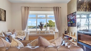 A modern living room with a leather sofa, a large window with curtains, and a flat-screen TV.