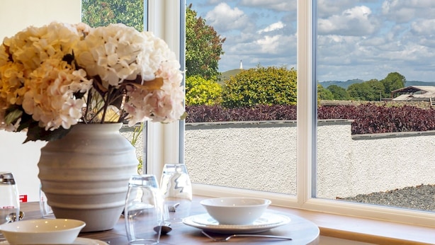 A dining table with a vase of flowers, clear glassware, and a view of a landscaped garden through large windows.