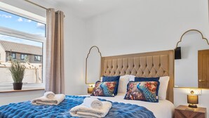 A modern bedroom with a tufted headboard, a large fluffy blue bedspread, and decorative pillows.