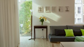 Ein modernes Wohnzimmer mit grauem Sofa, einem kleinen Tisch mit Blumenvase und einer Stehlampe.