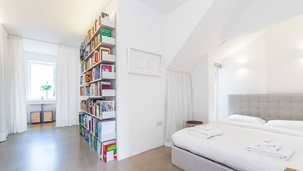 Ein modernes Schlafzimmer mit einem großen Bett, einem Bücherregal und einem Fenster mit Vorhängen.