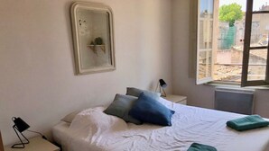Une chambre à coucher avec un lit, des oreillers, une table de chevet, une lampe et une fenêtre.
