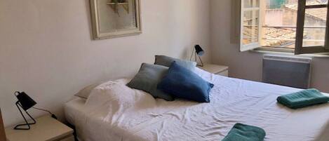 A bedroom with a bed, pillows, a nightstand, a lamp, and a window.