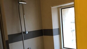 Une douche équipée d’un pommeau de douche à main et d’un robinet mural, une fenêtre avec vue et un mur à rayures noires et blanches.