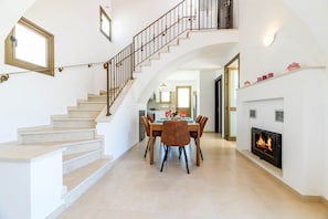 A spacious living area with a staircase, a dining table with chairs, and a fireplace.