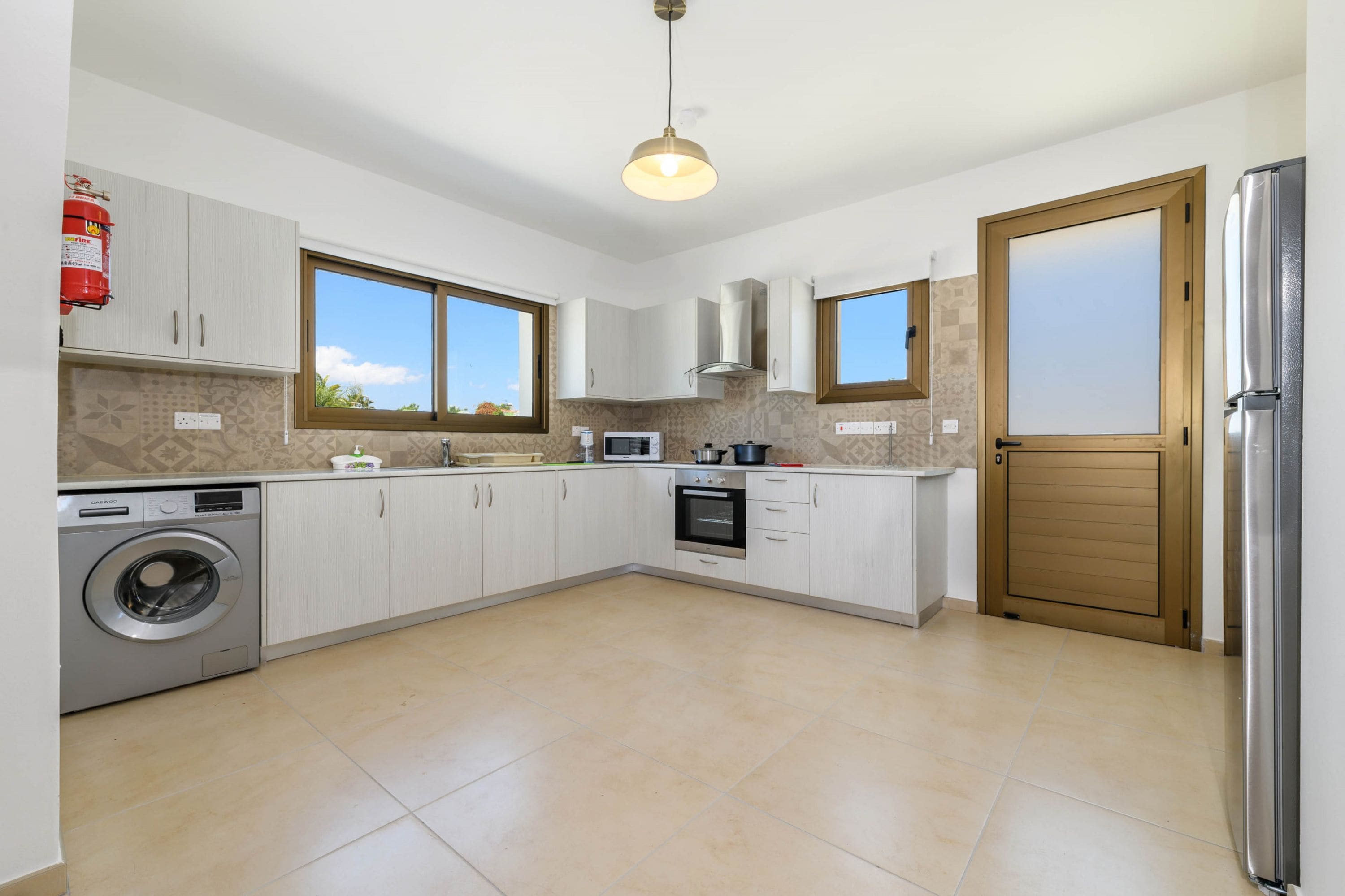 A modern kitchen with white cabinets, a built-in washing machine, a microwave, and a stainless steel refrigerator.