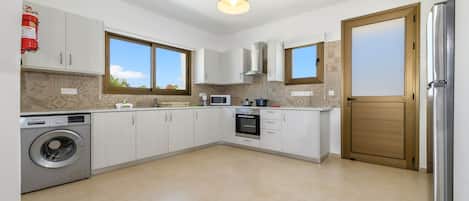 A modern kitchen with white cabinets, a built-in washing machine, a microwave, and a stainless steel refrigerator.