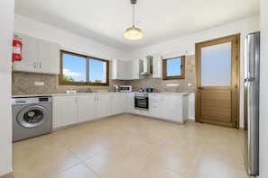 A modern kitchen with white cabinets, a built-in washing machine, a microwave, and a stainless steel refrigerator.