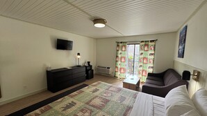 A bedroom with a bed, a dresser, a TV, a desk, a chair, and a window with curtains. - King Room With Balcony - NKB (Gatlinburg)