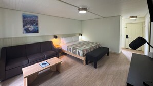 A bedroom with a bed, a sofa, a small table, a bench, and a painting on the wall. - King Room With Balcony - NKB (Gatlinburg)