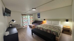 A bedroom with a bed, a desk, a chair, a bench, a TV, and a window with curtains. - King Room With Balcony - NKB (Gatlinburg)
