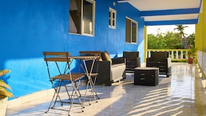 Une terrasse couverte avec des murs bleus, des meubles en osier et un sol carrelé.