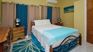 Une chambre à coucher avec un lit, des tables de chevet, une commode en bois, un tapis à motifs bleus et blancs et un tableau accroché au mur.