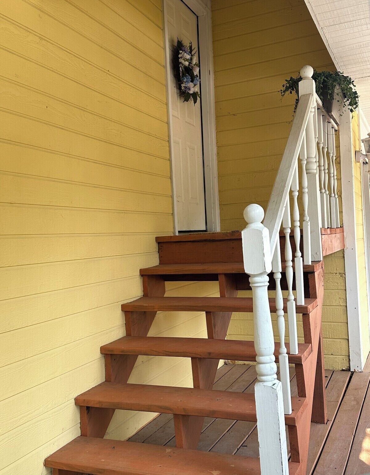 A wooden staircase with white balusters leading to a door with a floral wreath.