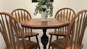 Une table à manger avec quatre chaises en bois, un vase avec des plantes vertes et un tableau encadré au mur.