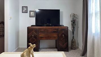 Ein Zimmer mit einem Holzkabinett, einem Fernseher darauf, einer Vase mit Trockenpflanzen und einer Skulptur auf dem Boden.