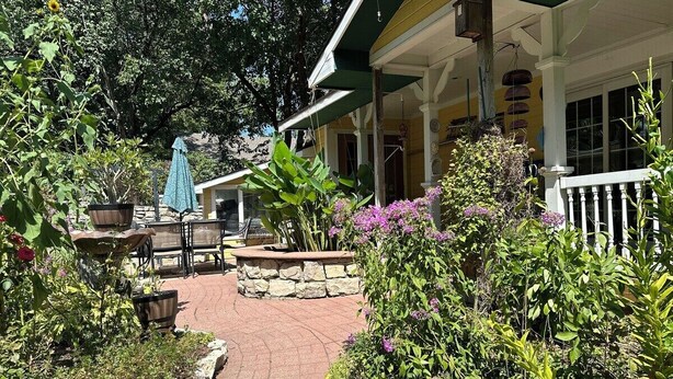 Un sentier de jardin menant à un bâtiment doté d’un porche, de jardinières en pierre et d’un espace salon extérieur.