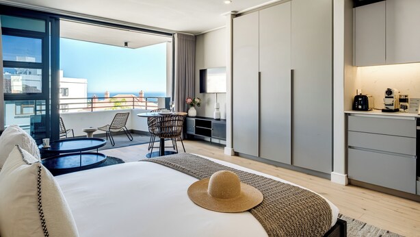 A modern hotel room with a balcony, a dining area, a kitchen, and a large bed. - Bantry Bay Retreat Ocean + Mountain Views (Cape Town)