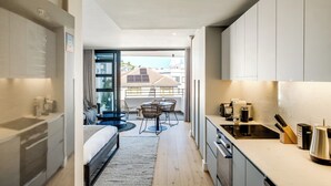 A modern hotel room with a kitchenette, a dining area with a table and chairs, a bed, and a view of the cityscape. - Bantry Bay Retreat Ocean + Mountain Views (Cape Town)