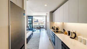 A modern kitchen with a built-in dishwasher, a coffee maker, and a kettle on the counter. There is a dining area with a table and chairs visible through the kitchen. - Bantry Bay Retreat Ocean + Mountain Views (Cape Town)