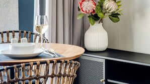 A modern room with a round dining table, a wicker chair, a white vase with flowers, a wine glass, and a flat-screen TV on the wall. - Bantry Bay Retreat Ocean + Mountain Views (Cape Town)