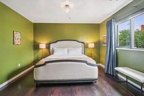 Une chambre à coucher avec un grand lit, deux lampes de chevet, un banc et une fenêtre avec des rideaux.