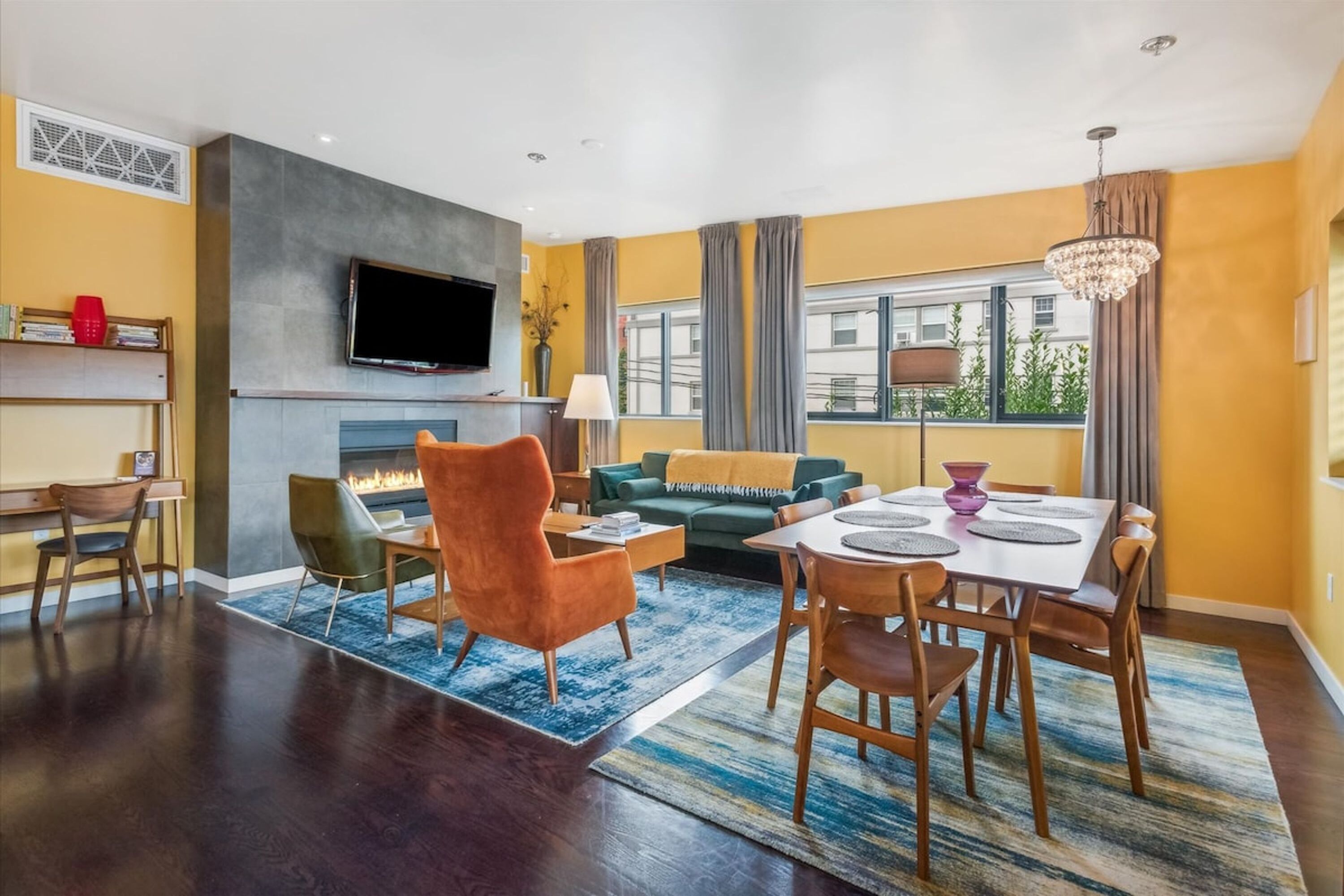 A modern living room with a fireplace, a television mounted on the wall, and a dining area with a table and chairs.