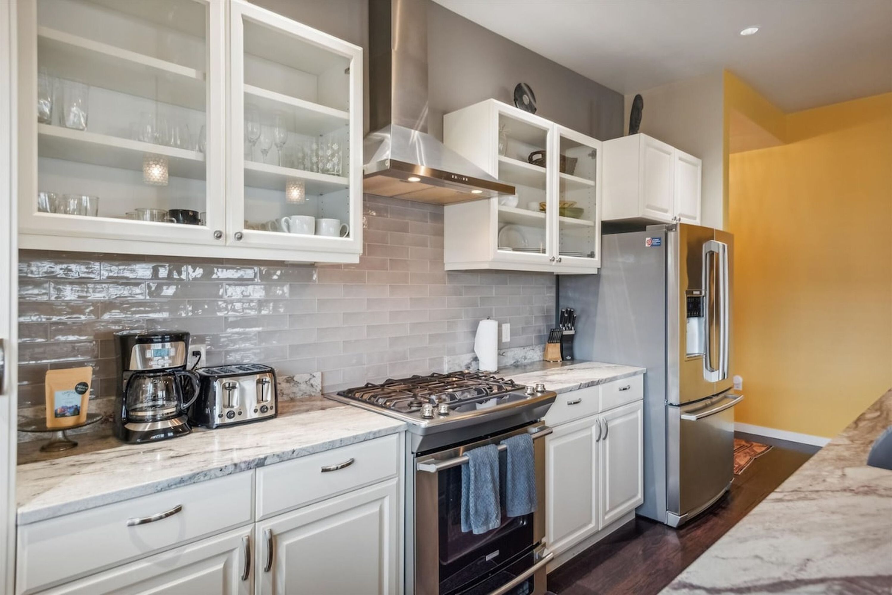 A modern kitchen with white cabinets, a stainless steel refrigerator, a gas stove, and a coffee maker.