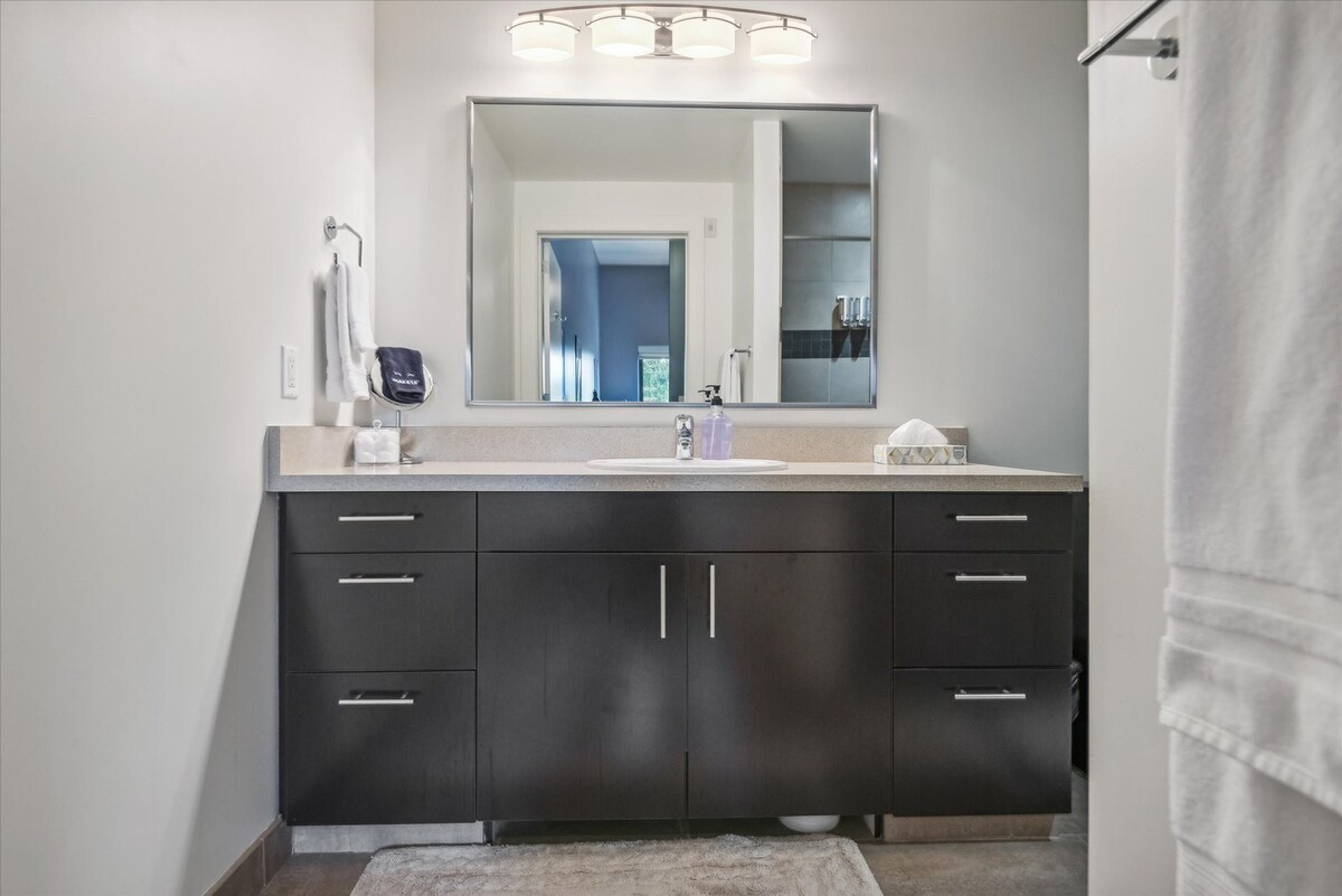 A modern bathroom with a large mirror, dark cabinets, and a light-colored countertop.