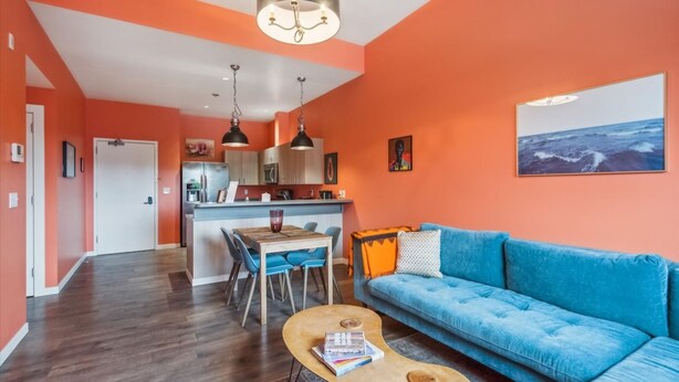 A modern living room with a blue sofa, wooden coffee table, and a dining area with a wooden table and chairs. - Chinook Suite - 203 in Portland (Portland)