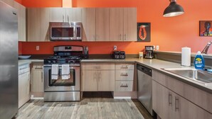 A modern kitchen with stainless steel appliances, wooden cabinets, and a bright orange wall. - Chinook Suite - 203 in Portland (Portland)